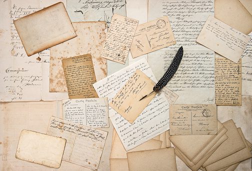 A collection of old handwritten letters and documents with a quill pen.