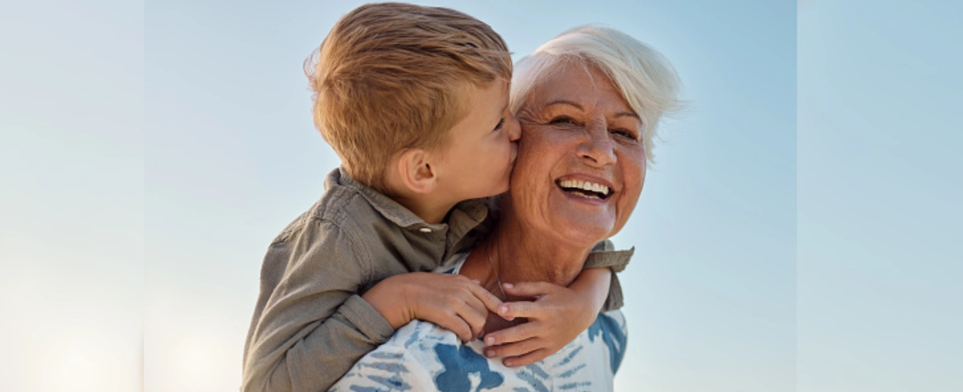Grandson kissing grandmother's cheek outdoors.