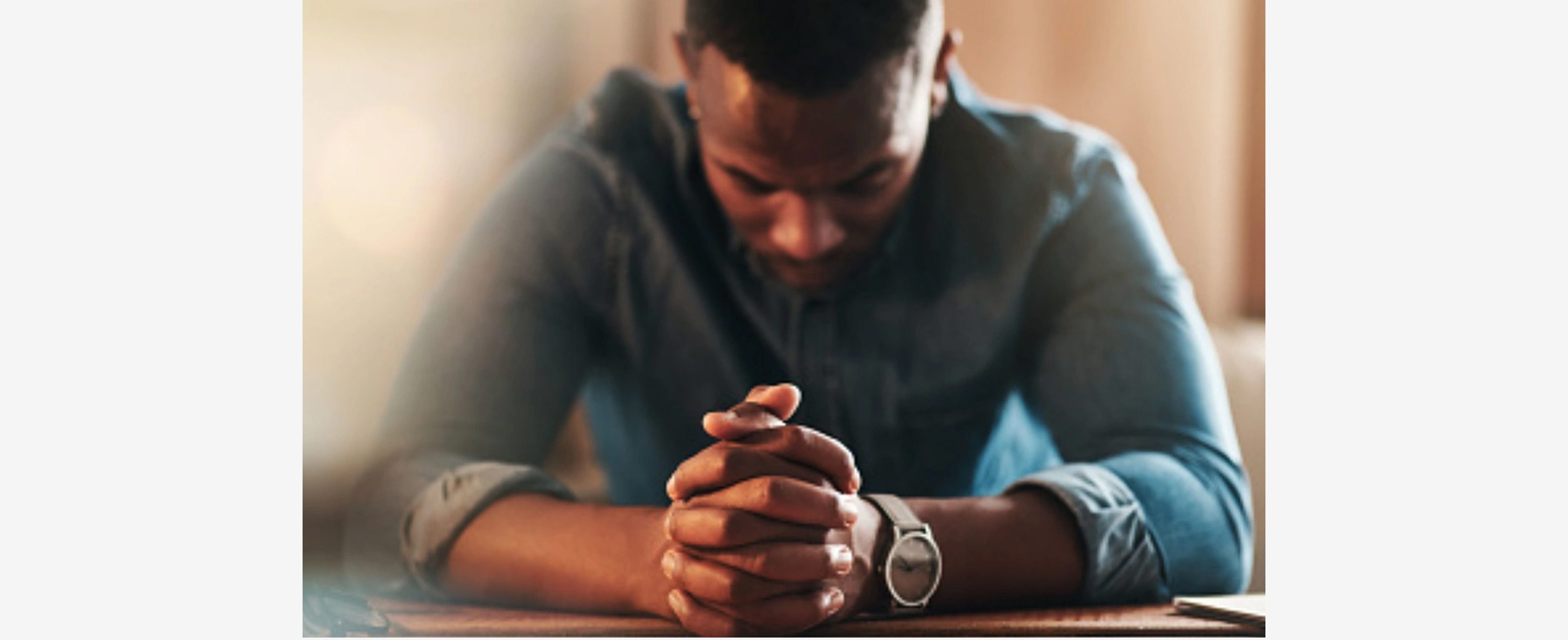 Man with clasped hands, head bowed in thought or prayer.